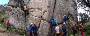 Una pareja escalando una gran pared de roca, parte del "Pack multiaventura en pareja en Madrid", con cascos y arneses, con árboles al fondo. - ForTwo - Planes para parejas