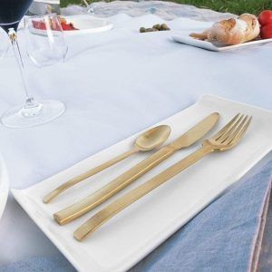 Un juego de cubiertos dorados reposa elegantemente sobre un plato blanco junto a copas de vino y pan, creando el ambiente ideal para el Picnic en Barcelona por sorpresa - Menú Mediterráneo. - ForTwo - Planes para parejas