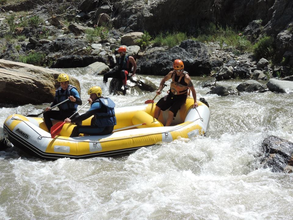 Aventureros con cascos y chalecos salvavidas navegan por los rápidos de un río rocoso cerca de Granada, dirigiendo una balsa inflable amarilla durante la experiencia Rafting en Granada - Canal de aguas bravas. - ForTwo - Planes para parejas