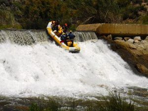 Un grupo maniobra hábilmente su balsa inflable amarilla por una cascada en medio de un exuberante follaje y terreno rocoso en el Rafting en Granada - Canal de aguas bravas. - ForTwo - Planes para parejas