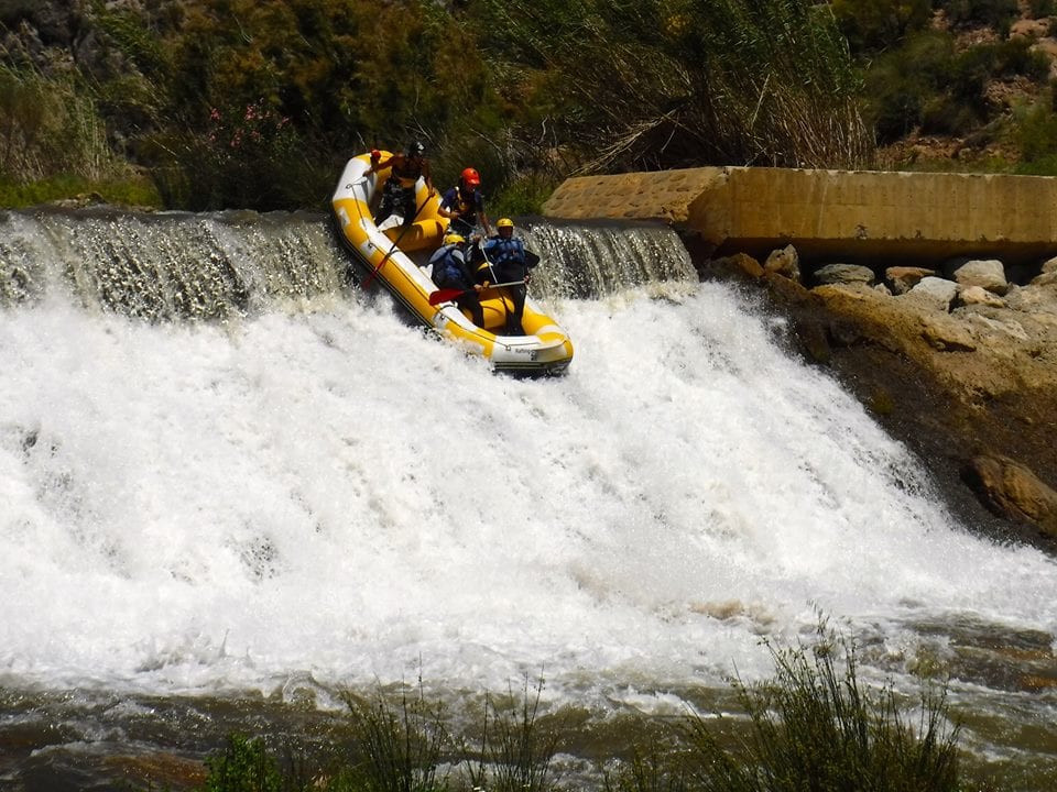 Un grupo maniobra hábilmente su balsa inflable amarilla por una cascada en medio de un exuberante follaje y terreno rocoso en el Rafting en Granada - Canal de aguas bravas. - ForTwo - Planes para parejas