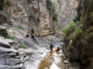 Los participantes de la experiencia "Barranquismo en Granada- Poqueira, en la Alpujarra" navegan por un cañón rocoso con cascos y equipo, entre escarpados acantilados y exuberante vegetación en la región de la Alpujarra cerca de Granada. - ForTwo - Planes para parejas