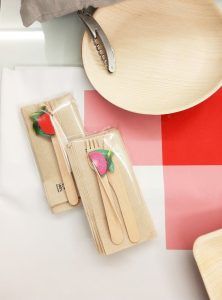 Los juegos de cubiertos de madera con decoración de frutas se colocan elegantemente sobre una mesa, combinados con un sacacorchos y un plato de madera, lo que hace que el Picnic en Barcelona - Menú InCity sea perfecto para una encantadora comida al aire libre. - ForTwo - Planes para parejas