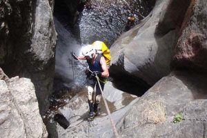 Equipada con equipo de protección, una persona desciende con destreza una cascada rocosa con cuerdas en el impresionante Barranco de Guardajamas durante la aventura Barranquismo en Granada. - ForTwo - Planes para parejas