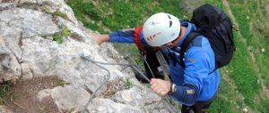Un escalador con chaqueta azul y casco aborda un acantilado rocoso utilizando cables y equipo en el Barranco de Guardajamas, parte de la aventura Barranquismo en Granada. - ForTwo - Planes para parejas