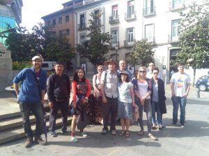 Un grupo de personas se reúne en un entorno urbano soleado, abrazados por el encanto de los pintorescos edificios y árboles del Albaicín, como parte del Tour por el Albaicín y Sacromonte de FeelTheCity. - ForTwo - Planes para parejas