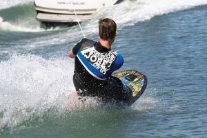 Un experto en wakeboard roza el agua, agarrado a una cuerda de remolque detrás de una veloz lancha, encarnando el espíritu surfear con "Una forma diferente de surfear, descubre el Kneeboard en Barcelona. - ForTwo - Planes para parejas