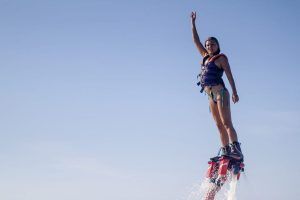 Volando sin esfuerzo sobre las cristalinas aguas de Barcelona con "Vuela sobre el agua en Hoverboard o Flyboard", una persona con chaleco salvavidas levanta un brazo triunfante contra el cielo azul claro. - ForTwo - Planes para parejas