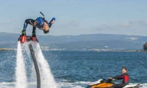 En las aguas de Barcelona, alguien realiza un emocionante backflip en el "Vuelo sobre el agua en Hoverboard o Flyboard en Barcelona", elevándose mientras otro observa con asombro desde su moto acuática. - ForTwo - Planes para parejas