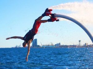 Una persona ejecuta un impresionante backflip en un flyboard del producto Vuela sobre el agua en Hoverboard o Flyboard en Barcelona, elevándose sobre aguas cristalinas con el icónico skyline de Barcelona y un cielo azul claro como telón de fondo. - ForTwo - Planes para parejas