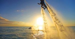 Alguien en un Hoverboard o Flyboard de "Vuela sobre el agua en Hoverboard o Flyboard en Barcelona" asciende sobre el océano al atardecer, reflejando los vivos colores de un crepúsculo barcelonés. - ForTwo - Planes para parejas