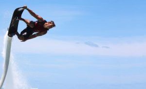 Una persona experta realiza un truco impresionante en "Vuela sobre el agua en Hoverboard o Flyboard en Barcelona", elevándose contra el cielo azul claro de fondo cerca de la ciudad. - ForTwo - Planes para parejas