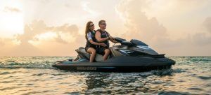 Una pareja experimenta "Surca las olas de Barcelona en moto acuática" mientras navegan entre las olas del océano al atardecer, recortadas por el horizonte de Barcelona contra un cielo nublado. - ForTwo - Planes para parejas
