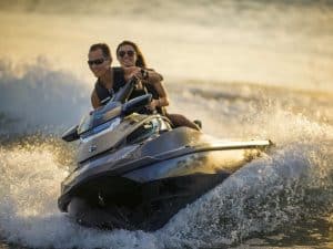 Dos personas disfrutan de un emocionante paseo en "Surca las olas de Barcelona en moto acuática", cortando las olas al atardecer cerca de las costas de Barcelona. - ForTwo - Planes para parejas