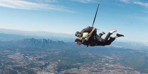 Dos personas experimentan el paracaidismo tándem desde 4000 metros con BCN SkyDive, disfrutando de impresionantes vistas de montañas y campos cerca de Barcelona. - ForTwo - Planes para parejas