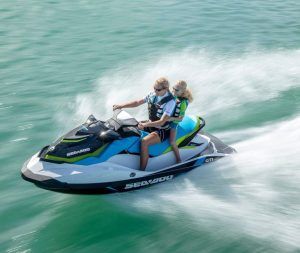 Dos personas disfrutan de un paseo en la "Surca las olas de Barcelona en moto acuática" por las cristalinas aguas azules, creando salpicaduras blancas en medio de suaves olas. - ForTwo - Planes para parejas