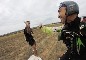 Dos paracaidistas en tierra chocan los cinco en un campo abierto bajo un cielo nublado, con el ánimo tan alto como si acabaran de experimentar una Paracaidismo en Barcelona desde 4000 metros - BCN SkyDive impresionante. - ForTwo - Planes para parejas