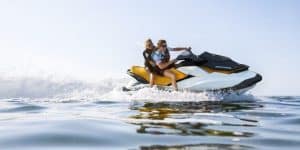 En una moto acuática amarilla y negra, dos personas se deslizan suavemente sobre aguas tranquilas bajo un cielo despejado, capturando las vibraciones soleadas de Barcelona con el Surca las olas de Barcelona en moto acuática. - ForTwo - Planes para parejas