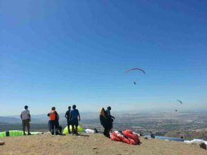 Aventureros listos para un emocionante vuelo en parapente en Granada despegan desde la cima de una colina, vibrantes parapentes se elevan sobre el impresionante telón de fondo del paisaje de Granada. - ForTwo - Planes para parejas