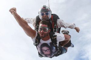 Dos personas practican paracaidismo en tándem, una de ellas en pose de Superman, ambas con gafas y contra un fondo nublado de Barcelona durante el Paracaidismo en Barcelona desde 4000 metros - BCN SkyDive. - ForTwo - Planes para parejas