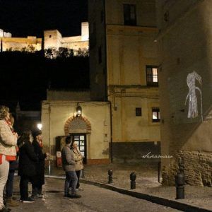 El Tour Conspiración en el Albaicín Granada encanta a los espectadores mientras la proyección de un vestido ilumina un edificio por la noche, con la majestuosa fortaleza del Albaicín brillando al fondo. - ForTwo - Planes para parejas