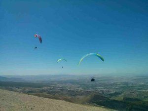 Tres planeadores de Vuelo en parapente en Granada se elevan con gracia sobre el impresionante paisaje de Granada, con un cielo azul claro y colinas distantes que realzan la fascinante vista. - ForTwo - Planes para parejas