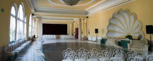 El salón de banquetes de la Habitación Doble y Circuito de Aguas Saludables en Balneario de Lanjarón presenta un fondo de conchas ornamentadas, hileras de sillas blancas, ventanas arqueadas y paredes amarillas. - ForTwo - Planes para parejas