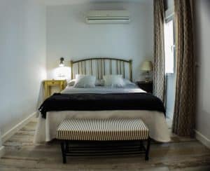 Acogedor dormitorio en Apartamento para 2 en el centro de Granada, cuenta con cama de matrimonio con cojines decorativos, mesitas de noche, lámpara y banco de rayas a los pies de la cama. - ForTwo - Planes para parejas
