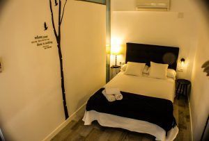 Acogedora habitación en el "Apartamento para 2 en el centro de Granada" con cama doble, cabecero negro, vinilo decorativo, lámpara y suelo de madera. Toallas cuidadosamente colocadas sobre la cama. - ForTwo - Planes para parejas