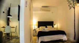 El elegante y moderno dormitorio del Apartamento para 2 en el centro de Granada cuenta con una cama doble, comedor, arte mural e iluminación suave en el vibrante corazón de la ciudad. - ForTwo - Planes para parejas