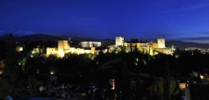 Disfrute de una cena para dos con vistas a la Alhambra en el Restaurante Estrellas de San Nicolás, con el complejo del castillo iluminado contra un paisaje montañoso bajo un cielo azul profundo para una experiencia encantadora. - ForTwo - Planes para parejas