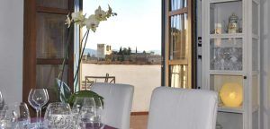 El comedor del Estrellas de San Nicolás luce una mesa preparada para "Cena para dos con vistas a la Alhambra", adornada con una orquídea y que ofrece impresionantes vistas de la Alhambra y las montañas a través de puertas abiertas. - ForTwo - Planes para parejas