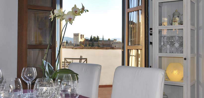 El comedor del Estrellas de San Nicolás luce una mesa preparada para "Cena para dos con vistas a la Alhambra", adornada con una orquídea y que ofrece impresionantes vistas de la Alhambra y las montañas a través de puertas abiertas. - ForTwo - Planes para parejas