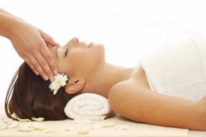 En el tranquilo entorno de Granada, una persona disfruta de un relajante masaje de cabeza durante una sesión de Masaje Mindfulness para 2 personas, con una flor en el pelo y pétalos esparcidos alrededor. - ForTwo - Planes para parejas