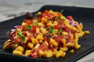 Sashimi en cubos con mango en cubos, adornado con microvegetales, se sirve hermosamente en un plato negro en el Restaurante Carmen El Agua en Granada del Menú Al Ándalus. - ForTwo - Planes para parejas