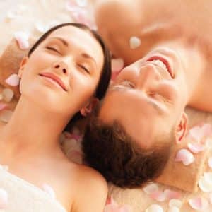 Una pareja disfruta de un Masaje Relajante para 2 por BorealRelax, con toallas bajo la cabeza y rodeados de pétalos de rosas rosadas. - ForTwo - Planes para parejas