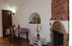 Encantadora habitación en Guadix con mesa, sillas, TV pequeña, chimenea de ladrillo y decoración rústica. Perfecto para "Una noche en cueva romántica de turismo rural. - ForTwo - Planes para parejas