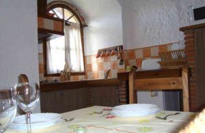 Una acogedora cocina con azulejos a cuadros, una mesa de comedor y ventanas con cortinas evocan el encanto de "Una noche en cueva romántica de turismo rural (Guadix)". Los utensilios sobre la encimera invitan a preparar una comida caliente en este acogedor espacio. - ForTwo - Planes para parejas