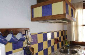 Esta encantadora cocina evoca la sensación de "Una noche en cueva romántica de turismo rural (Guadix)" con su protector contra salpicaduras de azulejos azules y amarillos, tazas y utensilios colgantes, un pequeño fregadero y una ventana adornada con cortinas transparentes: una escapada perfecta de turismo rural. - ForTwo - Planes para parejas