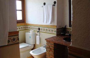 Un acogedor baño diseñado al estilo de "Dos noches en cueva romántica con hammam y masaje (Guadix)" cuenta con inodoro, bidé, toallero y lavabo sobre una encimera de ladrillo, todo ello elegantemente adornado con un borde floral. - ForTwo - Planes para parejas