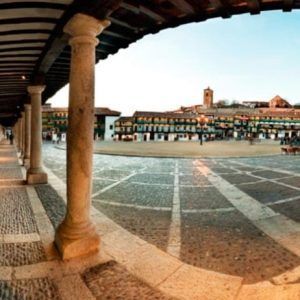 Una vista panorámica de la Plaza Mayor de Chinchón, con pasarelas arqueadas y adoquines, realza el encanto de la Bodega del Nero. Aquí podrás disfrutar de una "Visita guiada a Bodega del Nero con tren turístico y degustación de 3 vinos". - ForTwo - Planes para parejas