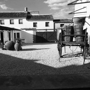 Una imagen en blanco y negro muestra el patio rústico de Bodega del Nero, completo con barriles, un carro y un edificio. - ForTwo - Planes para parejas