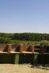Una zona de cocina de ladrillo al aire libre tiene vistas a un exuberante bosque verde bajo un cielo azul claro, creando el entorno perfecto que recuerda a "Dos noches en cueva romántica con hammam y masaje (Guadix). - ForTwo - Planes para parejas