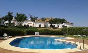 Disfrute de una relajante piscina al aire libre con tumbonas, vegetación y un edificio en la cima de una colina bajo un cielo azul claro después de experimentar el "Circuito Hammam con Masaje" en Cuevas del Abuelo José en Guadix. - ForTwo - Planes para parejas