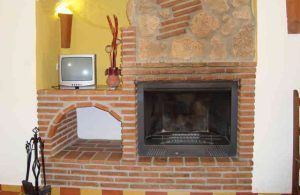 Una acogedora chimenea de ladrillo con un pequeño televisor sobre una estantería, rodeada de una decoración rústica como la de "Dos noches en cueva romántica con hammam y masaje (Guadix). - ForTwo - Planes para parejas