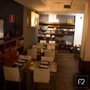 Un restaurante acogedor con iluminación tenue, decoración moderna y mesas cuidadosamente dispuestas con sillas blancas. Las estanterías de madera realzan el encanto del ambiente del Restaurante Ruta del Azafrán, donde podrás disfrutar del "Menú Sabores en Restaurante Ruta del Azafrán frente a la Alhambra. - ForTwo - Planes para parejas