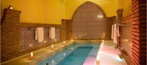 Este acogedor spa ofrece una estadía de dos noches en Dos noches en cueva romántica con hammam y experiencia de masaje, con un arco de azulejos, piscina cubierta, cálida iluminación amarilla, velas y lujosas toallas que adornan las paredes. - ForTwo - Planes para parejas