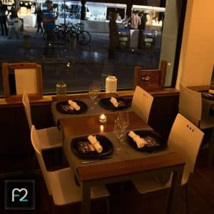 En medio de un ambiente acogedor, "Degustación en Restaurante Ruta del Azafrán frente a la Alhambra" cuenta con mesas iluminadas con velas, servilletas dispuestas artísticamente y una vista al aire libre de la Alhambra complementada con el animado paisaje del mercado nocturno. - ForTwo - Planes para parejas