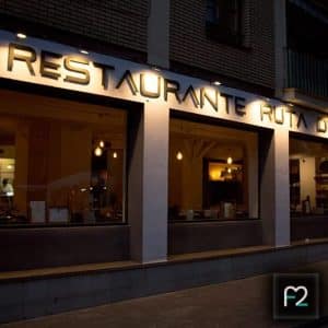 El exterior del Restaurante Ruta del Azafrán muestra un letrero luminoso, "Restaurante Ruta", con su cálida iluminación interior visible a través de las ventanas. Los huéspedes pueden disfrutar de un Menú Sabores único en el Restaurante Ruta del Azafrán a pocos pasos de las impresionantes vistas de la Alhambra. - ForTwo - Planes para parejas