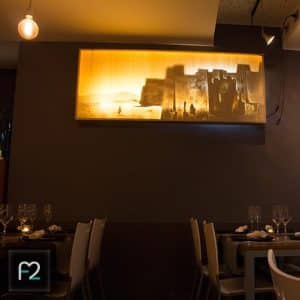 El interior poco iluminado del Restaurante Ruta del Azafrán, que ofrece el Menú Sabores, exhibe arte mural brillante de una fortaleza que se asemeja a la Alhambra, con mesas de comedor cuidadosamente dispuestas que crean una atmósfera acogedora. - ForTwo - Planes para parejas
